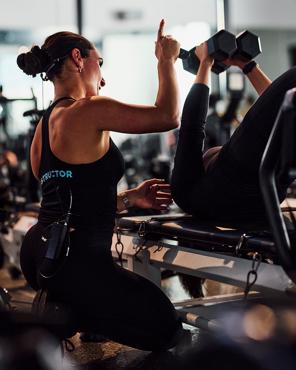 Instructor beside a member lifting a dumbbell on a reformer